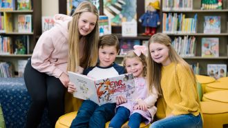 Four youth pose with a book inside Wright Library