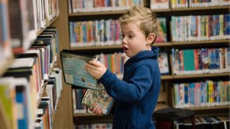 Young boy exclaims while pulling materials from library shelf.