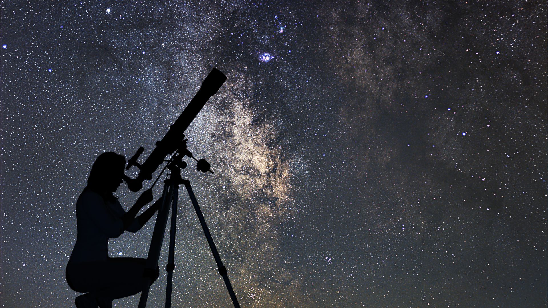 Sillouette of person peering through a telescope at the night sky.